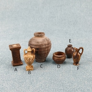 Può includere: Sei vasi in ceramica in miniatura di diverse forme e dimensioni. I vasi sono di colore marrone e beige con una finitura rustica. I vasi sono disposti in fila su una superficie testurizzata blu chiaro.