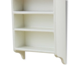 May include: White wall-mounted shelf with three shelves. The shelf has a simple design with a slightly curved bottom edge.