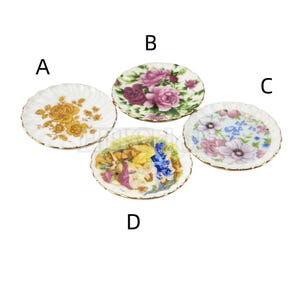 May include: Four decorative ceramic plates with floral and nature-inspired designs. The plates are white with gold trim and feature different floral patterns, including roses, anemones, and a fairy scene.