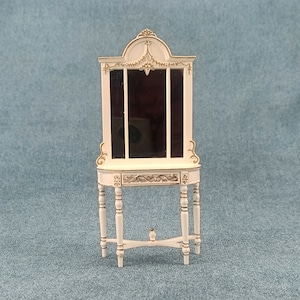 May include: White vanity table with a gold-trimmed mirror and ornate details. The table has a small shelf and four legs with decorative accents.