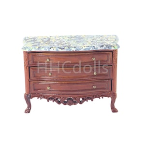 May include: A miniature wooden dresser with three drawers and a marble top. The dresser has ornate carvings and gold-colored handles.