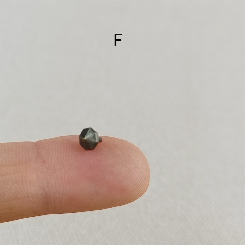 Puede incluir: Un peque&ntilde;o tachuela de metal gris oscuro en forma de estrella con una punta.