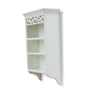 May include: White wooden wall shelf with three shelves and a decorative top. The shelf has a scalloped bottom edge.