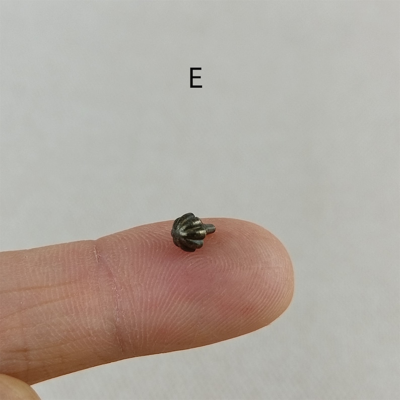 Puede incluir: Un peque&ntilde;o bot&oacute;n de metal plateado con una parte superior decorativa acanalada. El bot&oacute;n tiene un solo pasador peque&ntilde;o en la parte posterior.