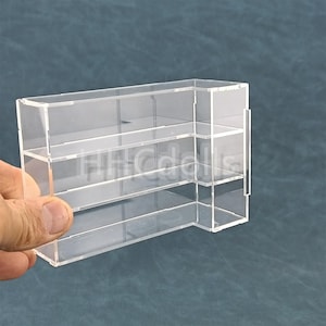 Puede incluir: Una estantería de exhibición de acrílico transparente con cuatro estantes. La estantería está inclinada y tiene un panel lateral.