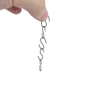 May include: A chain of six black metal S-shaped hooks hanging from a finger.