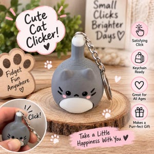 Puede incluir: Un llavero fidget clicker con forma de gato gris y blanco, cuerpo redondeado, orejas puntiagudas y cadena de metal. El gato tiene una cara impresa con ojos negros, bigotes y mejillas rosadas. El dispositivo emite un clic al presionarlo.