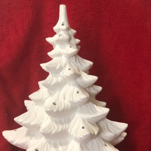 Può includere: Un albero di Natale in ceramica bianca con una superficie testurizzata e fori per le luci. L'albero ha una base con un design decorativo.