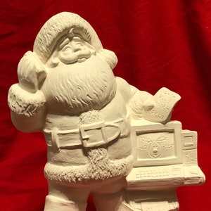 May include: White ceramic figurine of Santa Claus holding a computer and a stack of papers. The computer screen reads "North Pole Alert". The papers have text such as "Christmas Wishes" and "Santa Claus List".