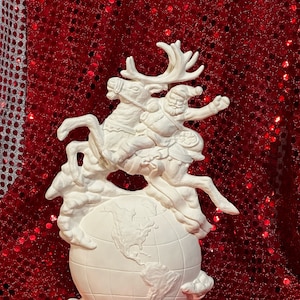 May include: White ceramic figurine of Santa Claus riding a reindeer over a globe. The globe is detailed with continents and a base with holly leaves.