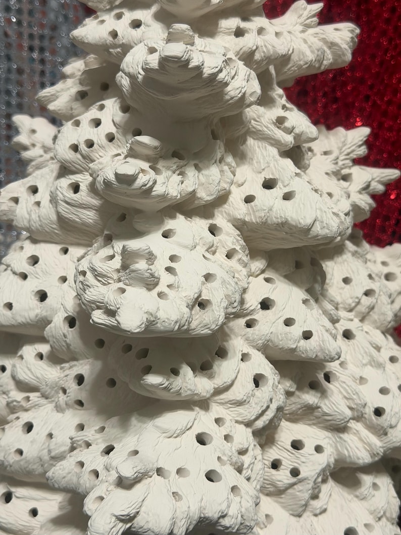 Pu&ograve; includere: Primo piano di un albero di Natale in ceramica bianca con una superficie strutturata e porosa. L'albero ha un design dettagliato e stratificato con numerosi piccoli fori, creando un aspetto decorativo unico. L'albero &egrave; non verniciato e pronto per la personalizzazione.