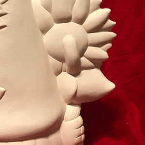 May include: White ceramic figurine of a gnome holding a sunflower. The gnome is wearing a hat and has a long beard. The sunflower is facing away from the viewer.