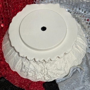 Pu&ograve; includere: Una ciotola decorativa in ceramica bianca con bordo smerlato e foro centrale. La ciotola presenta un motivo floreale in rilievo strutturato nella parte inferiore. La ciotola &egrave; probabilmente per scopi decorativi.