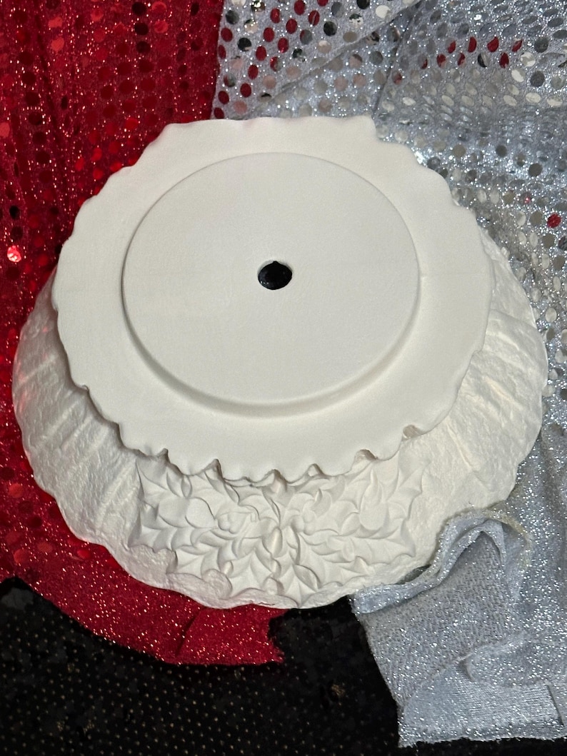 Pu&ograve; includere: Una ciotola decorativa in ceramica bianca con bordo smerlato e foro centrale. La ciotola presenta un motivo floreale in rilievo strutturato nella parte inferiore. La ciotola &egrave; probabilmente per scopi decorativi.