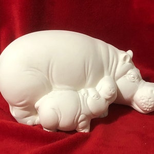 Könnte beinhalten: Weiße Keramikfigur einer Mutter-Flussrosses mit einem Baby-Flussross, das sich an sie kuschelt. Das Mutter-Flussross liegt mit dem Kopf zur Seite gedreht, während das Baby-Flussross den Betrachter ansieht.