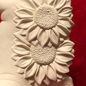 May include: White ceramic sculpture of two sunflowers with raised details. The sculpture is unfinished and ready to be painted.