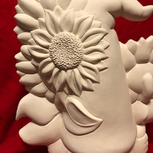 May include: White ceramic gnome figurine with a sunflower on its head. The gnome is wearing a hat and has a beard. The sunflower is detailed with petals and a center.