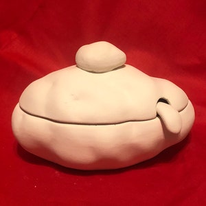 May include: White ceramic container with a lid shaped like a rounded rock. The container has a small opening on the side.