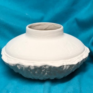 May include: White ceramic vase with a textured, ruffled rim. The vase has a wide, shallow bowl shape.