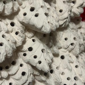 Pu&ograve; includere: Primo piano di un oggetto decorativo bianco e strutturato con un design a forma di albero. L'oggetto presenta una serie di piccoli fori scuri su tutta la sua superficie. L'estetica generale &egrave; organica e dettagliata, suggerendo un articolo fatto a mano.