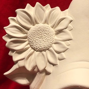 May include: White ceramic figurine of a sunflower with a detailed center and petals. The sunflower is attached to a stem and leaves.