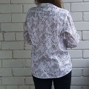 May include: A white button-down shirt with a black floral pattern. The shirt is worn with dark blue jeans and black heeled sandals.