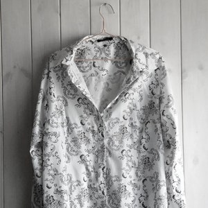 May include: A white long-sleeved button-up shirt with a black and white floral pattern.