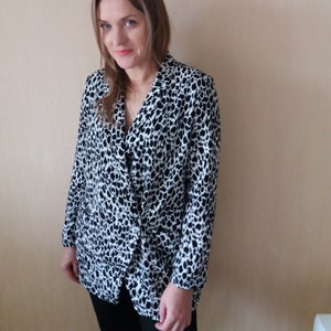Könnte beinhalten: Ein schwarzer und weißer Leopardenmuster-Blazer mit langen Ärmeln und einem V-Ausschnitt.