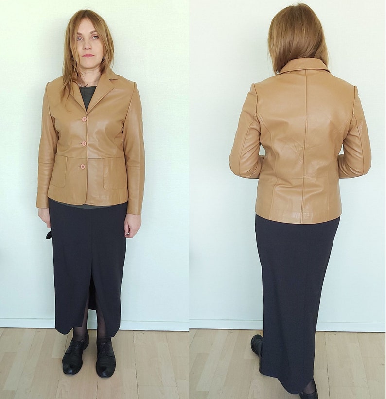 May include: A tan leather jacket with a button closure and two pockets. The jacket is worn over a black skirt.