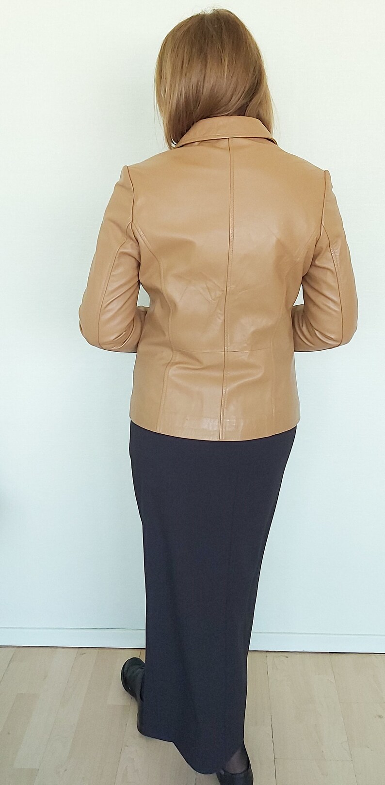 May include: A tan leather jacket with a long black skirt.