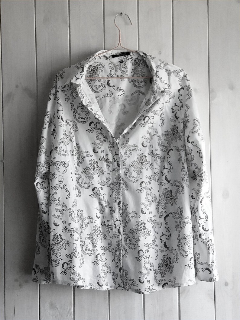May include: A white long-sleeved button-up shirt with a black and white floral pattern.