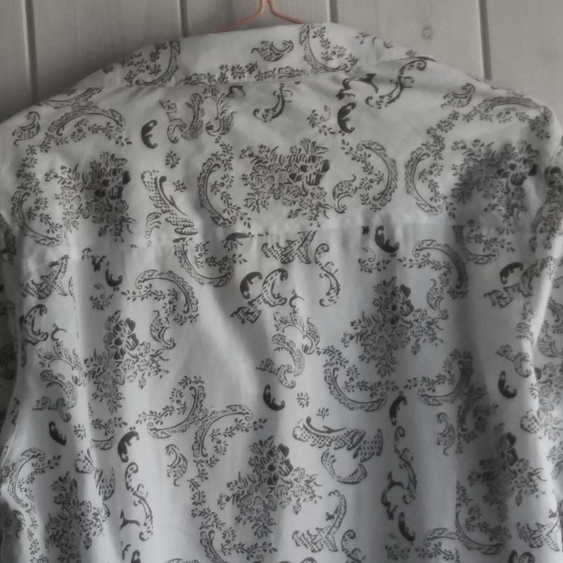 May include: White button-down shirt with a black floral pattern.