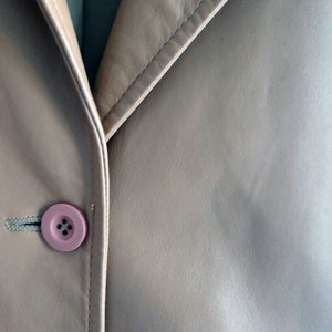 May include: A close-up of a beige leather jacket with a pink button.