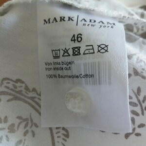 May include: White clothing label with black text that reads "MARK ADAM new york" and "46". The label also includes care instructions and the text "Von links b&uuml;geln Iron inside out 100% Baumwolle/Cotton".