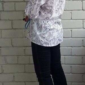 May include: A white button-down shirt with a black floral pattern. The shirt is worn with dark blue jeans and black heeled sandals.