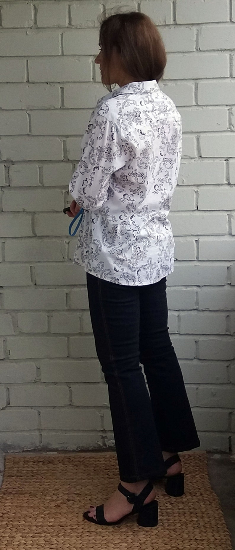 May include: A white button-down shirt with a black floral pattern. The shirt is worn with dark blue jeans and black heeled sandals.