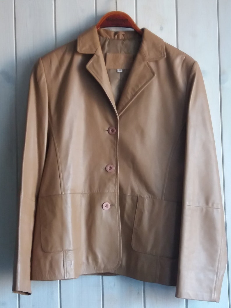 May include: A tan leather jacket with a button-up front and a single pocket on the left side.