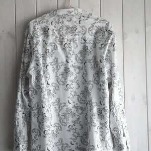 May include: A white long-sleeved button-up shirt with a black and white floral pattern.