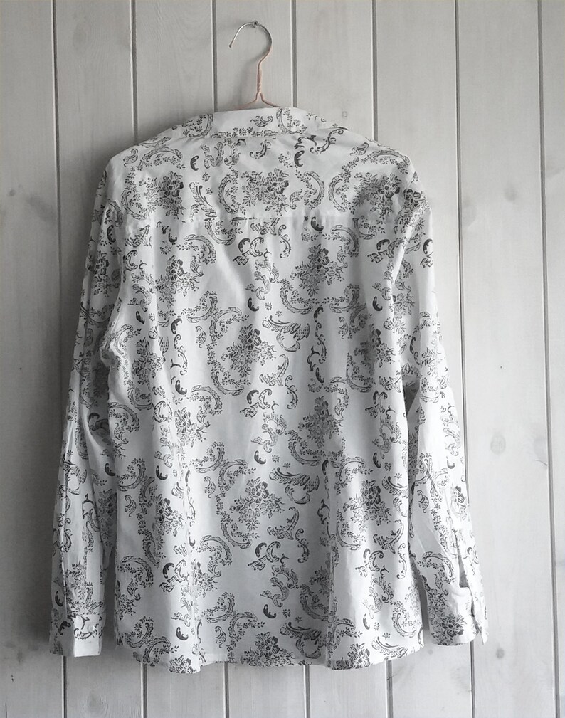 May include: A white long-sleeved button-up shirt with a black and white floral pattern.