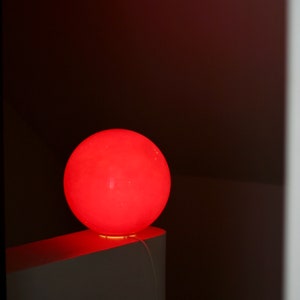 May include: A bright red spherical lamp sits on a white surface. The lamp is illuminated, casting a warm glow.