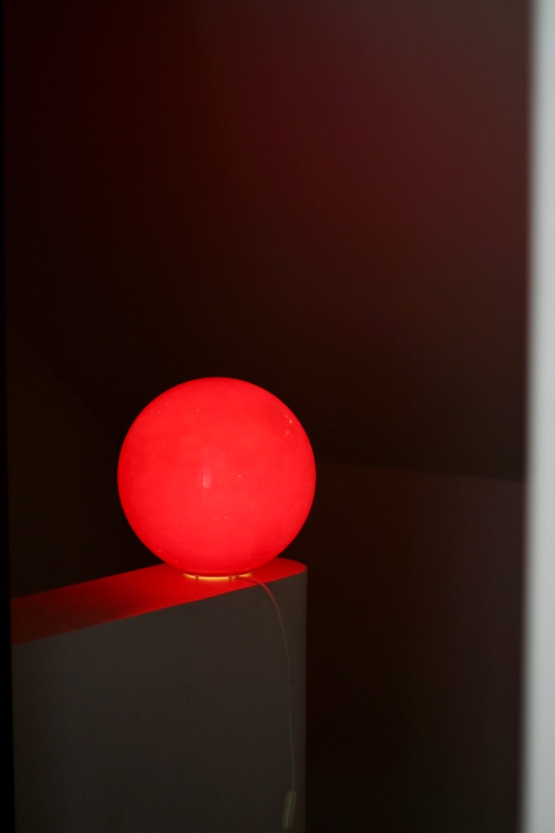 May include: A bright red spherical lamp sits on a white surface. The lamp is illuminated, casting a warm glow.