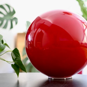 May include: A large, bright red, glossy, spherical object with a white base. The object is sitting on a dark surface.