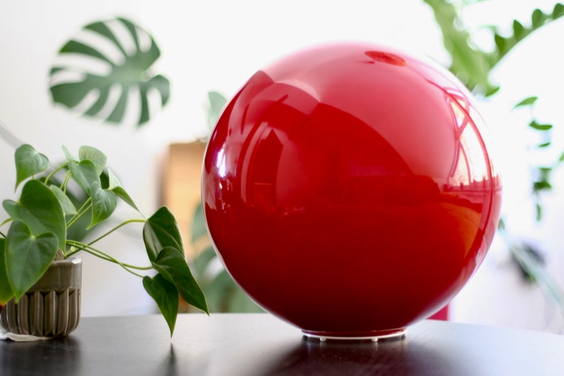 May include: A large, bright red, glossy, spherical object with a white base. The object is sitting on a dark surface.