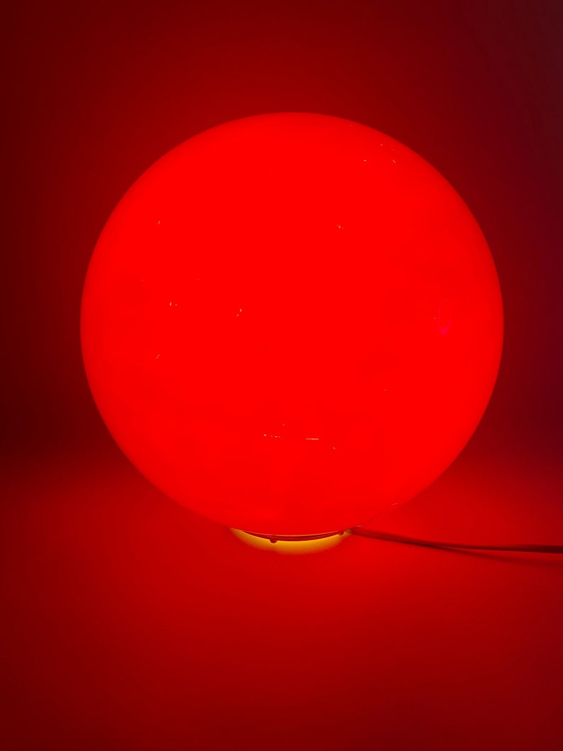 May include: A red glass sphere lamp with a yellow base.