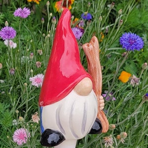 Handmade ceramic watering spike featuring a whimsical garden gnome with a red hat, white beard, and black shoes, set against a vibrant background of blooming flowers including daisies, cornflowers, and multicolored blossoms, ideal for artistic and eco-friendly plant hydration.