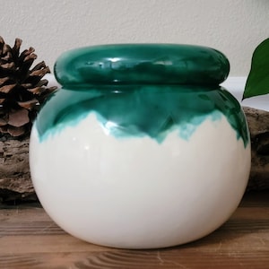 May include: A white ceramic planter with a green glazed top. The planter has a rounded shape and a smooth, glossy finish.