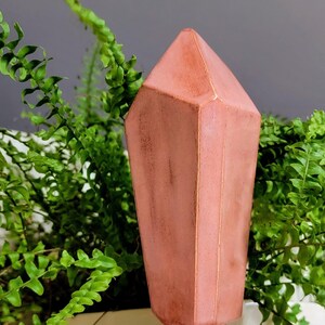 Handmade ceramic watering spike designed as a translucent pink, faceted crystal, delicately positioned amidst green fern leaves, providing a striking contrast and perfect for stylish and eco-friendly indoor plant care.
