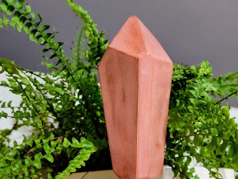 Handmade ceramic watering spike designed as a translucent pink, faceted crystal, delicately positioned amidst green fern leaves, providing a striking contrast and perfect for stylish and eco-friendly indoor plant care.