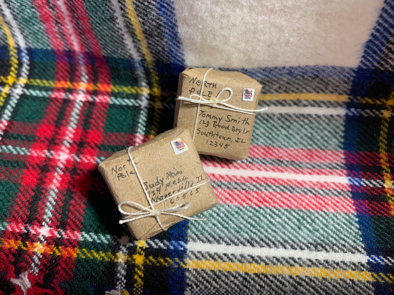 May include: Two small brown packages wrapped in twine with handwritten addresses to "North Pole" on a red and green plaid background. The packages are addressed to "Tommy Smith" and "Judy Mini".