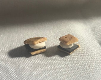 Może przedstawiać: Dwa mini s'mores wykonane z brązowych ciastek graham, białej pianki marshmallow i czarnej czekolady.